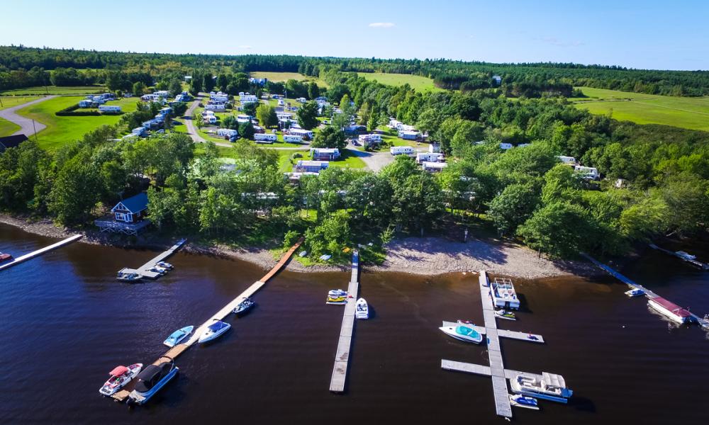 aerial shot of a dock on a river with boats and a lush green camping site behind it